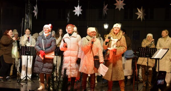 Wspólne kolędowanie podczas Wigilii Oświęcimskiej na Rynku Głównym w Oświęcimiu – występ zespołów i mieszkańców na scenie, świąteczna atmosfera, zimowy wieczór.