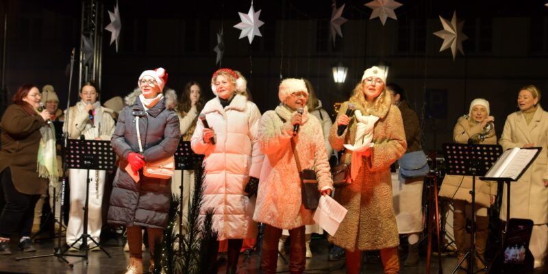 Wspólne kolędowanie podczas Wigilii Oświęcimskiej na Rynku Głównym w Oświęcimiu – występ zespołów i mieszkańców na scenie, świąteczna atmosfera, zimowy wieczór.