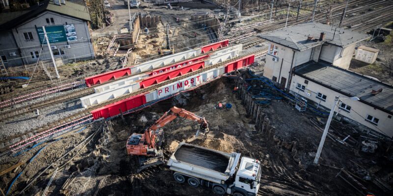 Budowa tunelu pod torami kolejowymi na ul. Wawelskiej w Bieruniu – widok z góry na konstrukcje odciążające firmy Primost Południe, prowadzone roboty ziemne, koparkę i ciężarówkę pracujące bezpośrednio pod czynnymi torami kolejowymi.