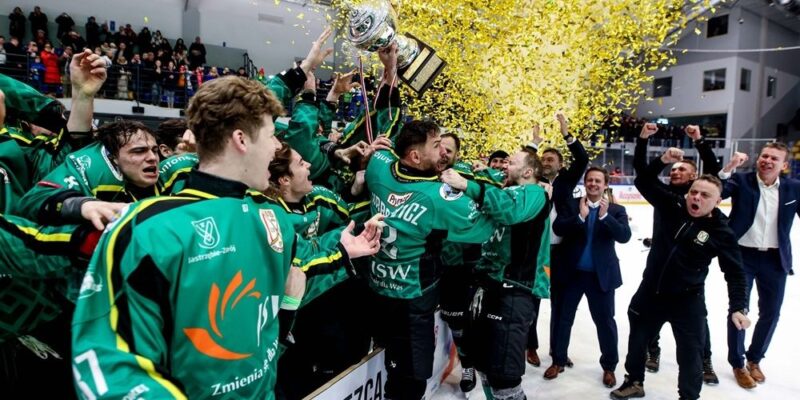 Hokeiści JKH GKS Jastrzębie świętują zdobycie TAURON Pucharu Polski – zawodnicy w zielonych strojach unoszą trofeum w górę, a nad lodowiskiem unoszą się złote konfetti po finale w Krynicy-Zdroju.