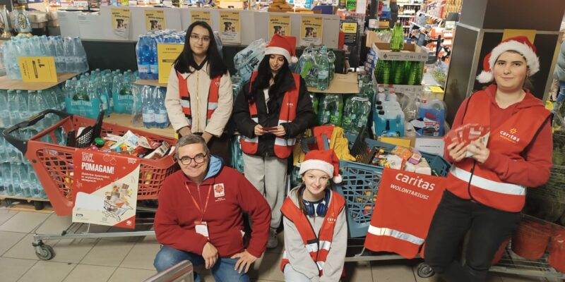 Wolontariusze Caritas Diecezji Bielsko-Żywieckiej podczas zbiórki „Tak Pomagam” w sklepie – młodzież i opiekun w czerwonych kamizelkach Caritas stoją przy koszach wypełnionych żywnością, zbieraną dla osób potrzebujących.