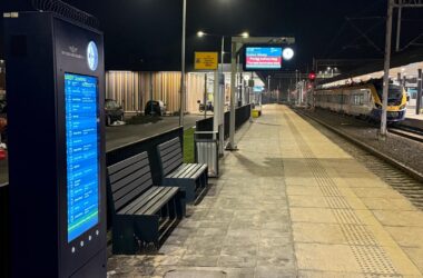 Nowe tablice dynamicznej informacji pasażerskiej i perony na dworcu kolejowym w Oświęcimiu w godzinach wieczornych; widoczny pociąg i oświetlony peron.