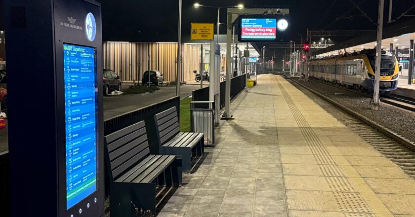 Nowe tablice dynamicznej informacji pasażerskiej i perony na dworcu kolejowym w Oświęcimiu w godzinach wieczornych; widoczny pociąg i oświetlony peron.