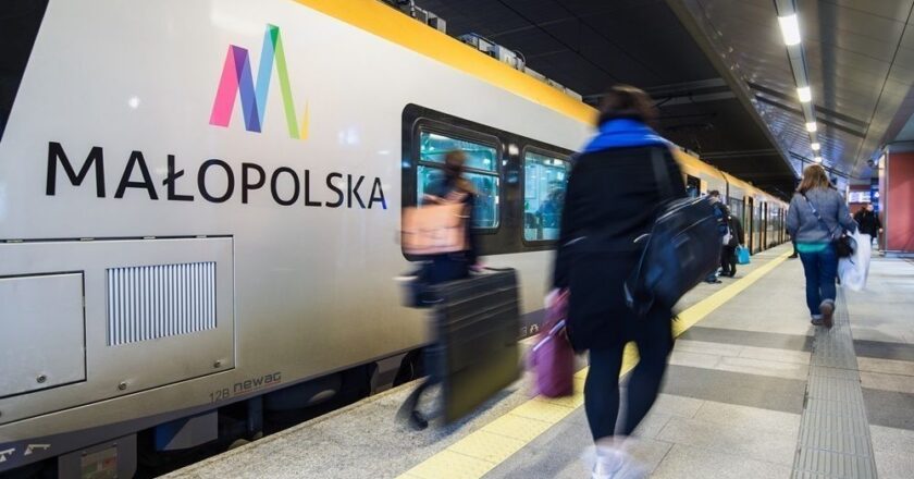 Pasażerowie wsiadający do pociągu Kolei Małopolskich na peronie podziemnego dworca, nowoczesny skład kolejowy z logo Małopolski, ruch i pośpiech w godzinach szczytu.