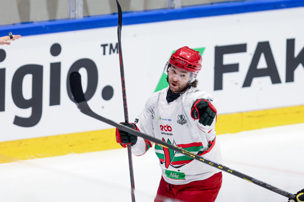 Zawodnik hokejowy ECB Zagłębie Sosnowiec w białym stroju cieszy się po zdobyciu bramki, wskazując kijem w kierunku trybun podczas meczu TAURON Pucharu Polski.