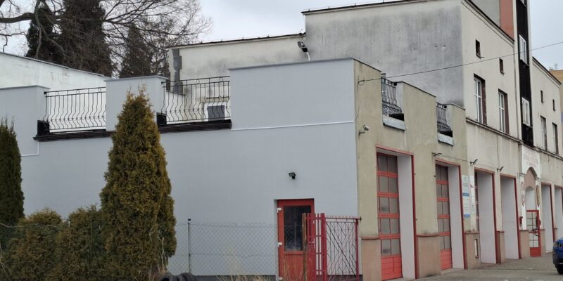 Budynek Ochotniczej Straży Pożarnej w Oświęcimiu po termomodernizacji – ocieplona elewacja strażnicy z czerwonymi bramami garażowymi, widok z zewnątrz zimą.