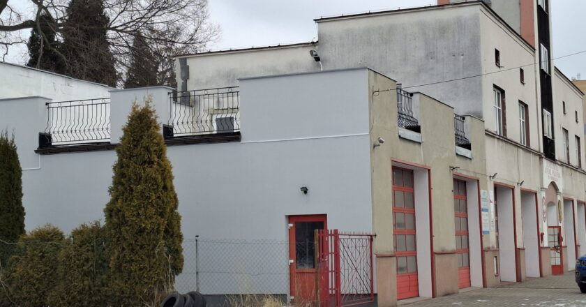 Budynek Ochotniczej Straży Pożarnej w Oświęcimiu po termomodernizacji – ocieplona elewacja strażnicy z czerwonymi bramami garażowymi, widok z zewnątrz zimą.