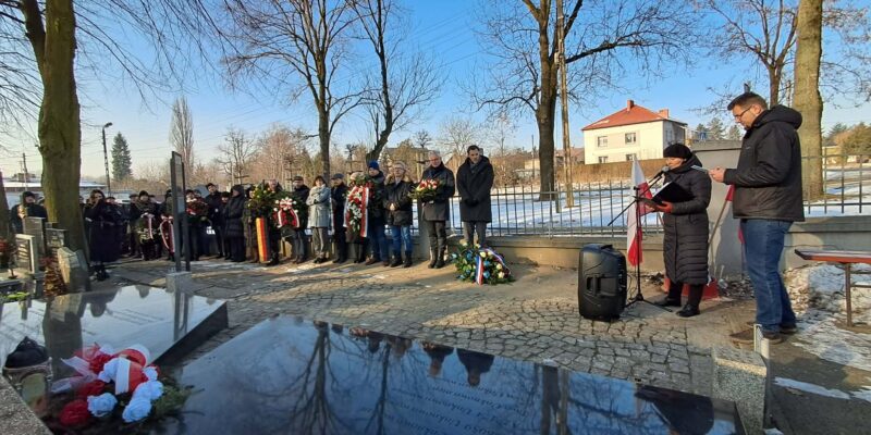 Uczestnicy uroczystości rocznicowych na cmentarzu w Brzeszczach składają wieńce i zapalają znicze przy mogile ofiar Marszu Śmierci z KL Auschwitz-Birkenau; w tle delegacje samorządowe, dyplomatyczne i mieszkańcy oddający hołd pomordowanym.