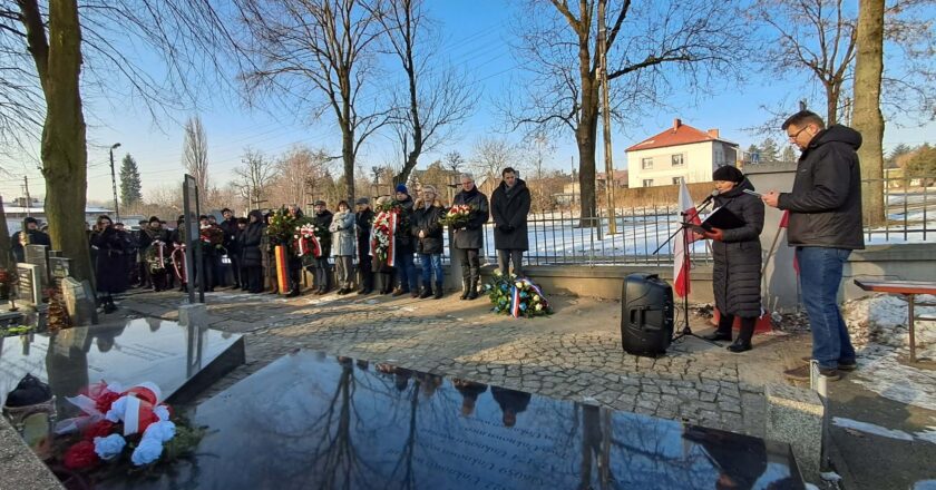 Uczestnicy uroczystości rocznicowych na cmentarzu w Brzeszczach składają wieńce i zapalają znicze przy mogile ofiar Marszu Śmierci z KL Auschwitz-Birkenau; w tle delegacje samorządowe, dyplomatyczne i mieszkańcy oddający hołd pomordowanym.