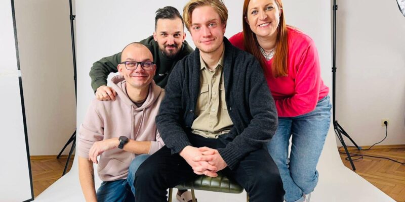 Uczestnicy projektu „Stories That Move” podczas nagrań w studiu – czworo młodych dorosłych siedzących i stojących przed białym tłem fotograficznym, uśmiechnięci, w nieformalnej atmosferze, przygotowani do realizacji materiałów edukacyjnych.