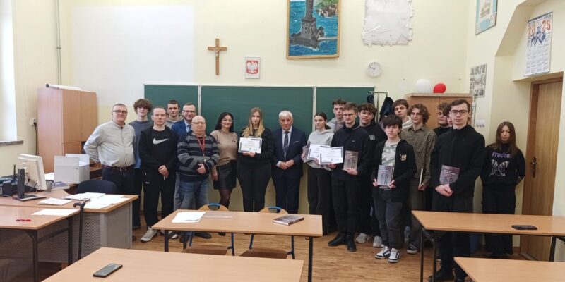 Uczniowie Powiatowego Centrum Kształcenia Technicznego i Branżowego w Oświęcimiu wraz z organizatorami i gośćmi pozują do wspólnego zdjęcia po konkursie wiedzy o historii KL Auschwitz-Birkenau; laureaci trzymają dyplomy i nagrody książkowe w sali lekcyjnej.
