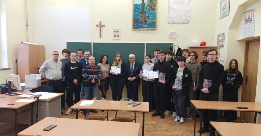 Uczniowie Powiatowego Centrum Kształcenia Technicznego i Branżowego w Oświęcimiu wraz z organizatorami i gośćmi pozują do wspólnego zdjęcia po konkursie wiedzy o historii KL Auschwitz-Birkenau; laureaci trzymają dyplomy i nagrody książkowe w sali lekcyjnej.