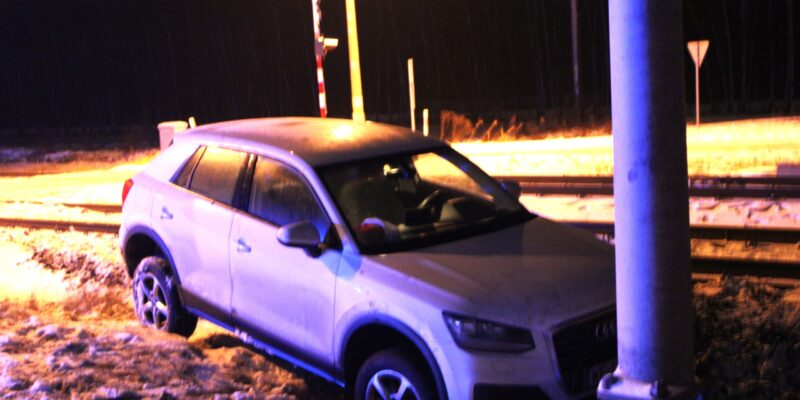 Samochód osobowy marki Audi po kolizji przy przejeździe kolejowym w Zatorze – auto stoi poza jezdnią, częściowo w śniegu, po uderzeniu w betonowy słup, nocne oświetlenie i widoczne tory kolejowe.