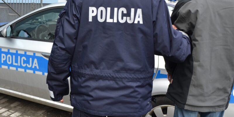 Policjant prowadzący zatrzymanego mężczyznę przy radiowozie policyjnym – interwencja Policji w Oświęcimiu.