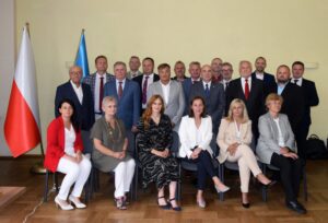 Radni Rady Miasta Oświęcim podczas wspólnego zdjęcia po sesji – grupa kilkunastu kobiet i mężczyzn w sali obrad, w tle flagi Polski i Unii Europejskiej.
