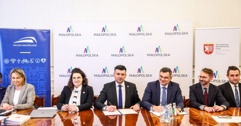 Podpisanie porozumienia o współpracy na rzecz bezpieczeństwa ruchu drogowego w Małopolsce – przedstawiciele władz województwa, Kolei Małopolskich i Wojewódzkiej Rady BRD siedzą przy stole konferencyjnym z logotypami Małopolski w tle.