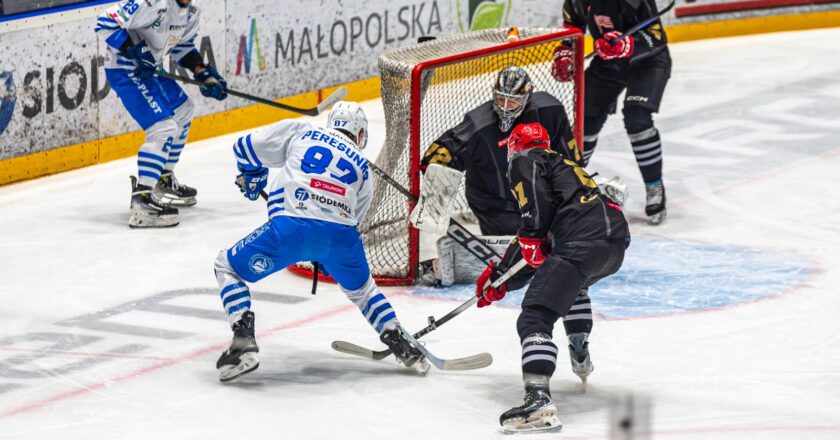 Akcja pod bramką Comarch Cracovii podczas meczu hokejowego z Unią Oświęcim. Ołeksandr Peresunko w biało-niebieskich barwach oddaje strzał z bliska, naciskany przez obrońców Cracovii, przed interweniującym bramkarzem krakowskiego zespołu. Dynamiczna sytuacja z derbów Małopolski w TAURON Hokej Lidze.