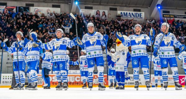 Hokeiści Unii Oświęcim dziękują kibicom na lodowisku po wysokim zwycięstwie, unosząc kije i bijąc brawo w stronę trybun wypełnionych fanami.