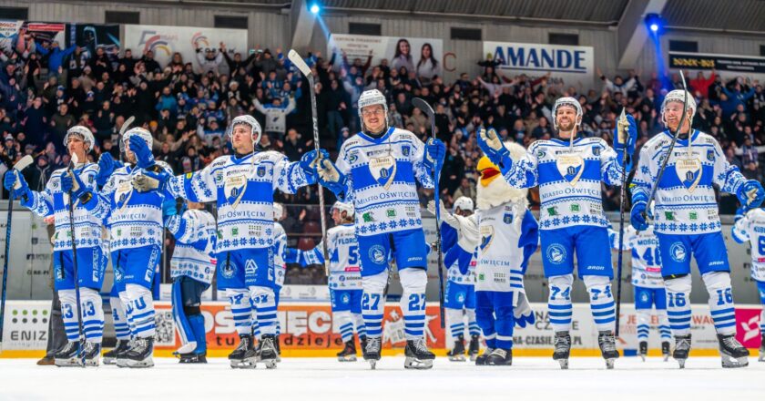 Hokeiści Unii Oświęcim dziękują kibicom na lodowisku po wysokim zwycięstwie, unosząc kije i bijąc brawo w stronę trybun wypełnionych fanami.