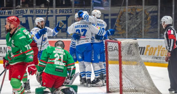 Radość hokeistów Unii Oświęcim po zdobytej bramce – biało-niebiescy świętują przy bramce Zagłębia Sosnowiec, bramkarz gości na kolanach.