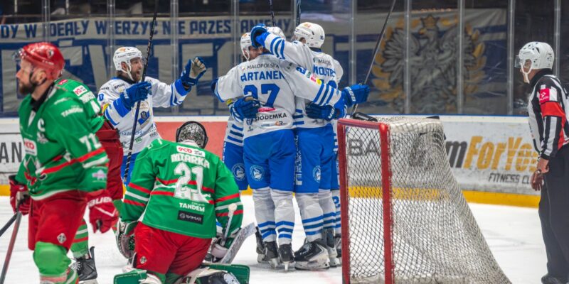 Radość hokeistów Unii Oświęcim po zdobytej bramce – biało-niebiescy świętują przy bramce Zagłębia Sosnowiec, bramkarz gości na kolanach.