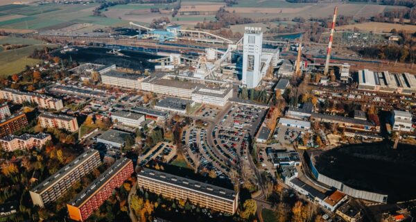 Widok z lotu ptaka na teren kopalni KWK Piast w Bieruniu – zabudowania przemysłowe, szyby, infrastruktura kolejowa oraz okoliczne osiedla mieszkaniowe i parkingi, w tle pola i tereny zielone.