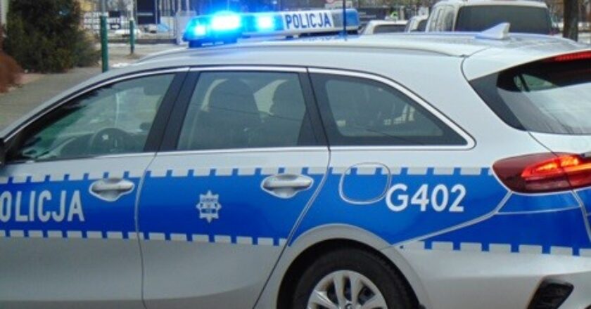 Radiowóz policyjny z włączonymi niebieskimi sygnałami świetlnymi, stojący przy ulicy.