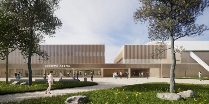 Wizualizacja nowej hali lodowej w Oświęcimiu – nowoczesny kompleks sportowy z jasną, drewnianą elewacją, przestronnym placem wejściowym i zielenią, po którym poruszają się mieszkańcy i sportowcy.